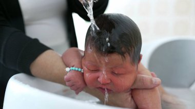 Newborn baby being lovingly cradled in a bath, with a hand gently resting on the baby's head for comfort and reassurance. baby's peaceful expression clipart