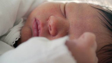 Yeni doğan bebek huzur içinde uyuyor. Yüzü ve eli yakın dinleniyor. Yumuşak ve güvenli bir ortamda, ilk yaşamın sıcaklığını, dinginliğini ve hassasiyetini yakalıyor.