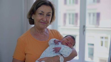 Büyükannesi yeni doğan torununu pencerenin kenarında beşikte, yumuşak doğal ışıkla yıkanmıştı. Bebeklerin barışçıl ifadeleri ve büyükannelerin sevgi dolu bakışları aralarındaki derin bağı vurgular.