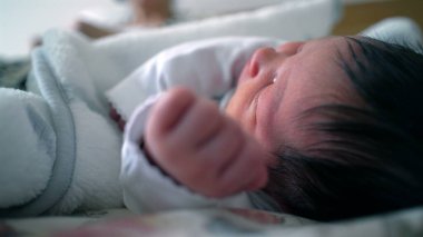 Yeni doğmuş bebek bir yatakta dinleniyor. Yüzlerine yakın bir elle yan yana uzanıyor. Sıcak ve güvenli bir ortamda, hassas bir uyku, rahatlık ve erken yaşam anı.