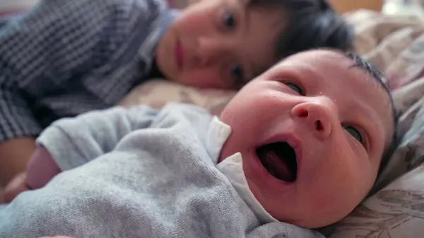 stock image Older brother lying next to newborn sibling, both sharing a quiet and close moment, with the brother gently holding the baby hand, illustrating the warmth and bond between siblings