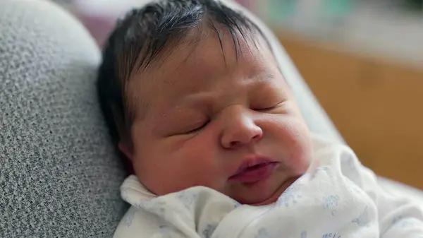 stock image Close-up of a newborn baby with dark hair, displaying a curious and slightly furrowed brow. The baby's intense gaze suggests deep thought or early concentration