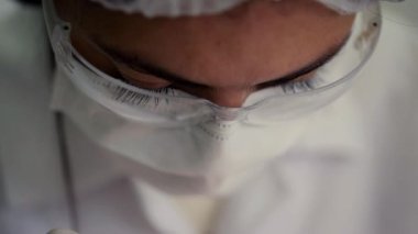 Bir diş hekiminin yüzüne yakın çekim, temiz ve modern bir klinik ortamında koruyucu gözlük ve maske takarken bir dişçi prosedürüne odaklanma