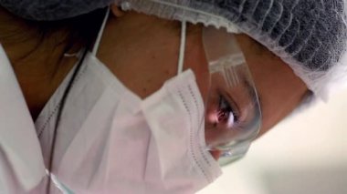 Bir diş hekiminin yüzüne yakın çekim, temiz ve iyi aydınlatılmış bir klinikte koruyucu gözlük ve maske takarken dikkatle bir diş prosedürüne odaklanma