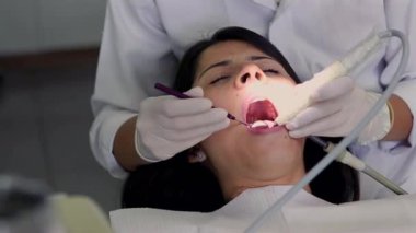 Diş tedavisi gören bir hastaya yakın çekim, özel aletlerle çalışan bir dişçi. Hasta ağzını açar açmaz dişçi prosedürü dikkatlice uygular.