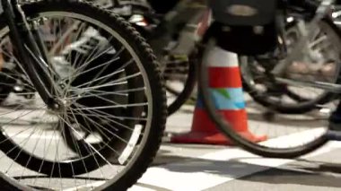 Bisiklet tekerlerinin şehir bisiklet etkinliği sırasında hareket halinde olduğu yakın plan, turuncu trafik konisi görünür, dinamik sokak sahnesi, hareket ve enerji, kentsel bisiklet, toplum aktivitesi, aktif yaşam tarzı