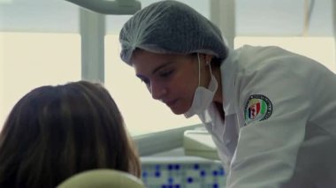 Diş hekimi, parlak, temiz ve profesyonel bir klinikte diş hekimi koltuğunda oturan bir hastayla konuşmak için eğildi.