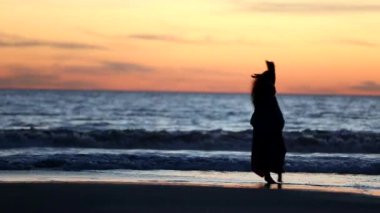 Karanlık çöktüğünde plajda özgürce dans eden bir insanın silueti, arka planda hafif dalgalar ve canlı bir gökyüzü, doğadaki özgürlük ve neşe duygusunu somutlaştırıyor.