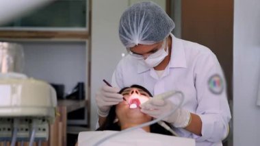 Diş hekimi, diş ameliyatı sırasında ağzı açık olan bir hastaya odaklanmış. Modern bir diş kliniğinde parlak ışıklar altında özel aletler ile profesyonel çalışmalar,