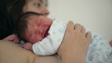 Annenin ağlayan bir bebeği kucağına alıp bebeğe güven ve sevgi sağlayan duygusal bağlantıya ve rahatlatıcı kucaklamaya odaklandığı yakın plan.