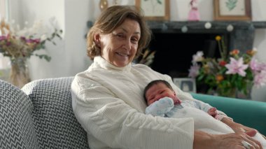 Büyükanne ve yenidoğan, bebek ile güvenli bir şekilde kollarına kurulmuş, nesiller boyu süren şefkatli sevgi ve bağlantıyı yansıtan, sessiz ve samimi bir anı paylaşıyorlar.