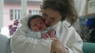 Büyükanne kollarında yeni doğmuş bebeğe şefkatle bakıyor, bebeği sıcak bir kucaklama, içten bir sevgi anı ve nesiller boyu derin bir bağ ile sarılıyor.
