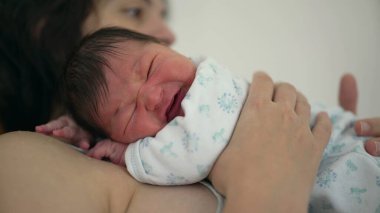 Annenin ağlayan bir bebeği kucağına alıp bebeğe güven ve sevgi sağlayan duygusal bağlantıya ve rahatlatıcı kucaklamaya odaklandığı yakın plan.