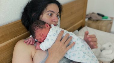 Yorgun bir anne, göğsünde yeni doğmuş bir bebekle, gözleri kapalı, huzurlu ama yorucu bir kucaklama içinde, derin bir bağ, sevgi ve erken anneliğin fiziksel taleplerini gösteriyor.