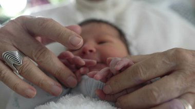 Büyükanne bebeklerin küçük ellerini nazikçe tutuyor, şefkat ve güven anı yakalıyor, sevgi dolu bir aile ortamında nesiller arasında paylaşılan samimi bir bağ. 