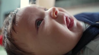 Meraklı bir ifadeyle sırtüstü uzanmış, dik dik bakan bir bebeğin yakın çekimi. Doğal ışıklandırma, bebek yüzünün ve teninin yumuşak dokusunu vurgular. 