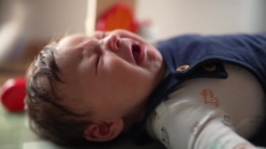 Bebek sırtüstü ağlıyor, gözleri sımsıkı kapalı, gözle görülür bir sıkıntı gösteriyor. Bebek, doğal ışıklandırmada rahatsızlığını ifade ediyor.