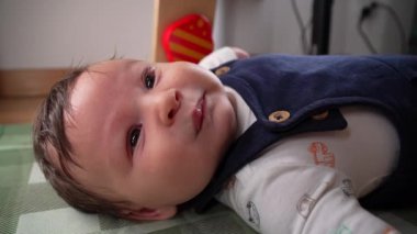 Bebek, ev ortamında bir paspasın üzerinde yatarken dikkat çekmeye başlıyor. Bebek, kollarını uzatarak rahatsızlık belirtileri gösterir. Doğal ortamdaki ilk duyguları ifade eder.