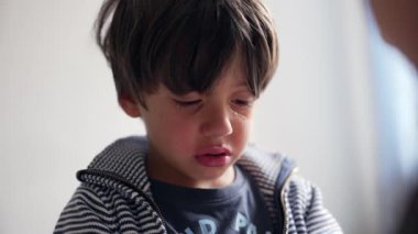 Çocuk ağladıktan sonra gözyaşlarıyla yansıyor, başı hafifçe eğik ve duygularını gösteriyor, kapalı alanda annesiyle olan duygularını işlerken sakin bir an..
