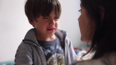 Genç bir çocuk ağlıyor, annesine bakarken görünür bir şekilde üzgün ve sıkıntılı. Bir anne ve çocuk arasındaki duygusal hassasiyet ve üzüntü anı.