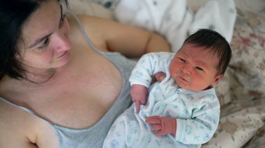 Yeni doğmuş bebek annesinin kollarında dinleniyor, sakin ama meraklı bir ifade sergiliyor. Hayatın ilk anları anne ve çocuk arasındaki derin bağlantıyı ve bakımı vurguluyor.