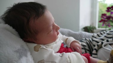 Yumuşak bir battaniyenin üzerinde dinlenen bebeğe yakın çekim, sakince bakmak, yakınlardaki bir pencereden gelen doğal ışık rahat bir ev ortamındaki huzurlu ortamı güçlendirir.