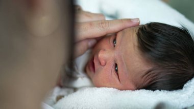 Anne yeni doğmuş bebeklerin yüzüne nazikçe dokunuyor, sakin ve rahat bir evde hassas ve samimi bir anı paylaşıyor. 