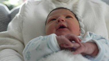 Yenidoğan sakince dinleniyor, sıcaklığa ve güvenliğe sarılmış, merakla bakıyor, huzurlu ve rahatlatıcı bir aile ortamında yeni hayatın masumiyetini ve mucizesini yansıtıyor.