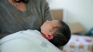 Yeni doğan bebek, annesinin kollarında huzur içinde dinleniyor. Yaşamın ilk evrelerinde sağlanan şefkat ve güvenliğin altını çiziyor. Erken yaşta annelik bağı.