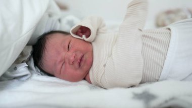 Yeni doğmuş bebek yatakta uzanıyor, esniyor ve yüzünü buruşturuyor. Bebekliğin hassas ve hassas bir anı. Yakın çekim, yeni doğan bir bebeğin hassas özelliklerini ve hassasiyetini vurgular.