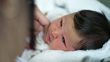 Anne yeni doğmuş bebeğin yüzüne nazikçe dokunuyor, sakin ve rahat bir evde hassas ve samimi bir anı paylaşıyor.
