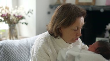 Büyükanne, yeni doğan bebeği nazikçe bir battaniyeye sardı. Huzurlu ve hassas bir anı paylaşıyor.