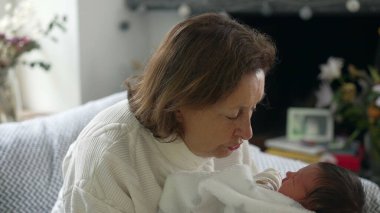 Büyükanne, yeni doğan bebeği nazikçe bir battaniyeye sardı. Huzurlu ve hassas bir anı paylaşıyor.