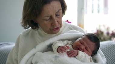 Büyükanne kucağında yeni doğmuş bir bebek, sevgiyle aşağı bakıyor, sıcak bir anı yakalıyor ve sıcak bir yuva kuruyor.