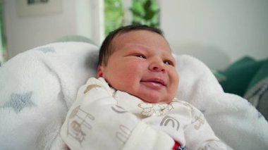 Yeni doğmuş bebek, yumuşak bir battaniyeye uzanmış neşeyle gülüyor. Huzurlu ve sevgi dolu bir yuva ortamında mutluluğu ifade ediyor.