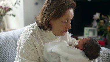 Büyükanne, yeni doğan bebeği nazikçe bir battaniyeye sardı. Huzurlu ve hassas bir anı paylaşıyor.
