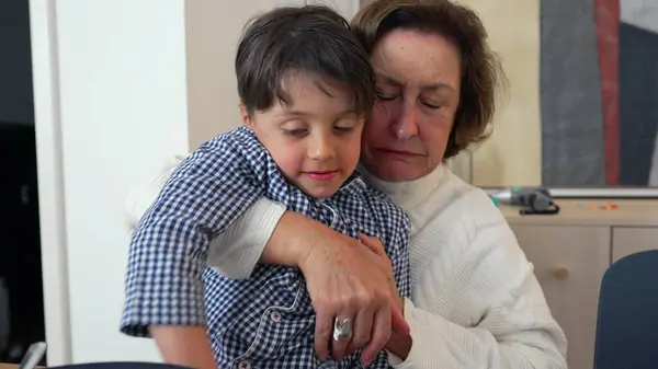 stock image Young boy affectionately kissing his grandmother on the cheek, sitting together at the dining table. Heartwarming display of family love and connection after sharing a meal