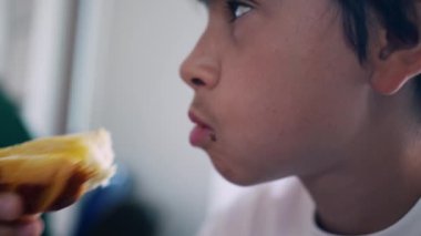 Küçük bir çocuğun bir parça ekmek yediği, elinde yemek tutarken bir ısırık aldığı, çerezinin tadını çıkarırken yüzünü ve ağzını gösterdiği yakın plan.