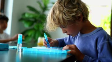 Renkli kalemle çizim yapmaya konsantre olan genç bir çocuk, yoğun bir şekilde işine odaklanmış, sakin bir evde çalışırken kalemi dikkatlice tutuyor.