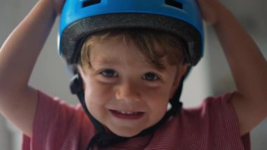 Mavi bir kask takan gülümseyen bir çocuk, her iki eliyle onu zevkle tutuyor, kayışı başarıyla bağladıktan sonra heyecan ve mutluluğu ifade ediyor. Saf çocukluk sevinci anı