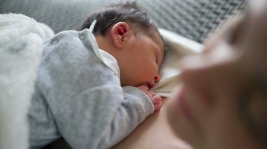 Yeni doğan bebek annesinin göğsünde huzur içinde uyuyor, yakın çekim, anne ve çocuk arasında paylaşılan rahatlık, güvenlik ve huzur dolu bağın altını çiziyor.