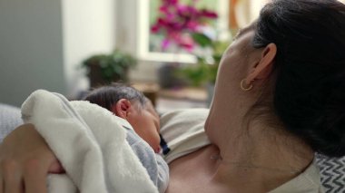 Anne yeni doğmuş bebeğini kucaklarken esniyor, erken ebeveynliğin yorgunluğunu ve hassas anlarını gösteriyor, zorluklara rağmen paylaşılan bağ ve sevgiyi vurguluyor