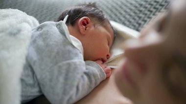Yeni doğan bebek annesinin göğsünde huzur içinde uyuyor, yakın çekim, anne ve çocuk arasında paylaşılan rahatlık, güvenlik ve huzur dolu bağın altını çiziyor.