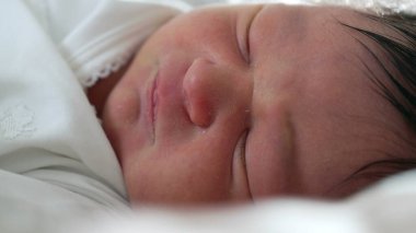 Yeni doğan bebek huzur içinde uyuyor, yüzü ve nazik ifadesiyle, yumuşak ve sıcak bir ortamda bir bebeğin erken yaşamının huzurlu ve huzurlu özünü yakalıyor.
