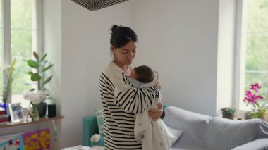 Anne, yeni doğmuş bebeğini nazikçe bir battaniyeye sarıp, anne ve çocuk arasındaki bağın ve sıcaklığın sessiz ve samimi anını yakalıyor.