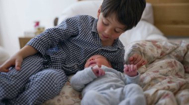 Büyük kardeş, yeni doğan kardeşlerini başlarından öperken, şefkatli bir ilgi ve şefkat anının altını çizerek kardeşler arasındaki güçlü bağı vurguluyor.