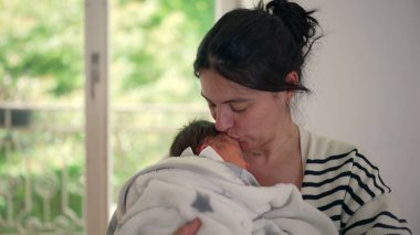 Anne, yeni doğmuş bebeğinin başını nazikçe öper, onları yakın tutarken, derin bir sevgi, ilgi ve anne ile çocuk arasındaki besleyici bağı gösterir.