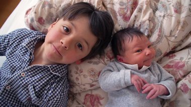 Çiçekli bir yatakta yenidoğan kardeşinin yanında yatan küçük çocuk, ömür boyu sürecek bir bağın başlangıcını ve bir yuva ortamındaki kardeşler arasındaki erken bağlantıyı resmediyor.