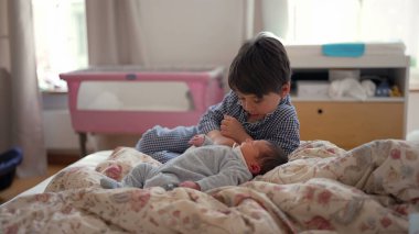 Ağabeyim, yeni doğan kardeşinin yanında, yatakta oturuyor, onları düşünceli bir ifadeyle gözlemliyor, kardeş ilişkisinin ilk aşamalarında sakin ve içsel bir anı yakalıyor.