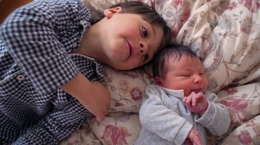 Çiçekli bir yatakta yenidoğan kardeşinin yanında yatan küçük çocuk, ömür boyu sürecek bir bağın başlangıcını ve bir yuva ortamındaki kardeşler arasındaki erken bağlantıyı resmediyor.